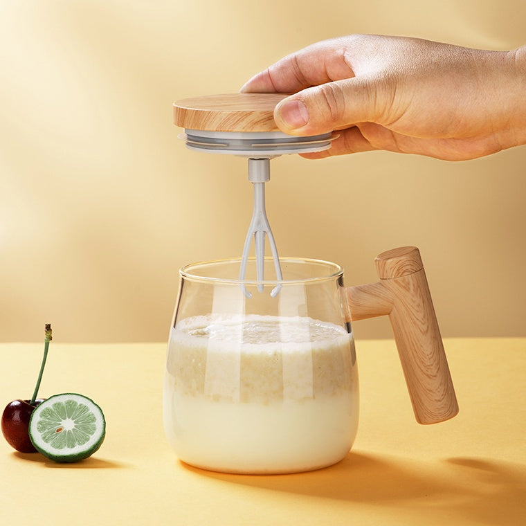 self stirring coffee mug with a person holding the mixing lid over a glass mug filled with a creamy beverage.