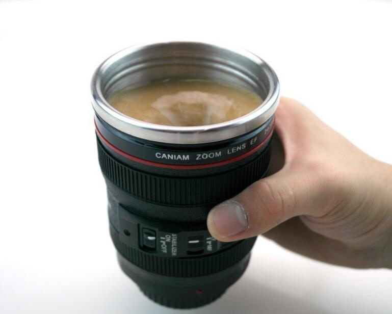 Camera lens self stirring mug filled with coffee held in a hand, showcasing unique design and self-stirring feature.