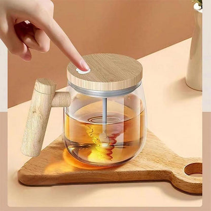 Self stirring coffee mug with a clear glass design and wooden lid, featuring a user pressing the button for effortless mixing.